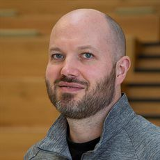 A bald man with a beard in a grey top